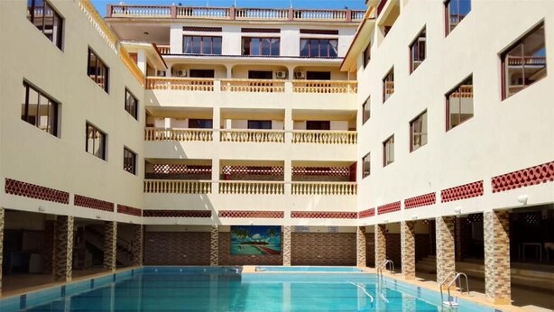 A swimming pool with a view of a multi-story building with balconies. - Darad Diani Hotel (Diani Beach)