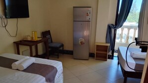 A hotel room with two beds, a refrigerator, a desk, a chair, a television, and a window with curtains. - Darad Diani Hotel (Diani Beach)