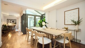 A modern dining area with a long table, six chairs, and a vase of flowers. - The Kensington End House (London)