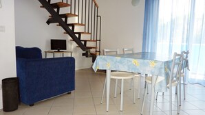 Ein Wohnzimmer mit einem blauen Sofa, einem Esstisch mit Stühlen, einem Fernseher und einer Treppe.