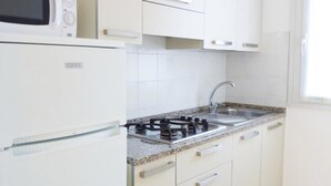 Kompakti keittiö, jossa on valkoiset kaapit, sisäänrakennettu mikroaaltouuni, kaasuliesi ja pesuallas.