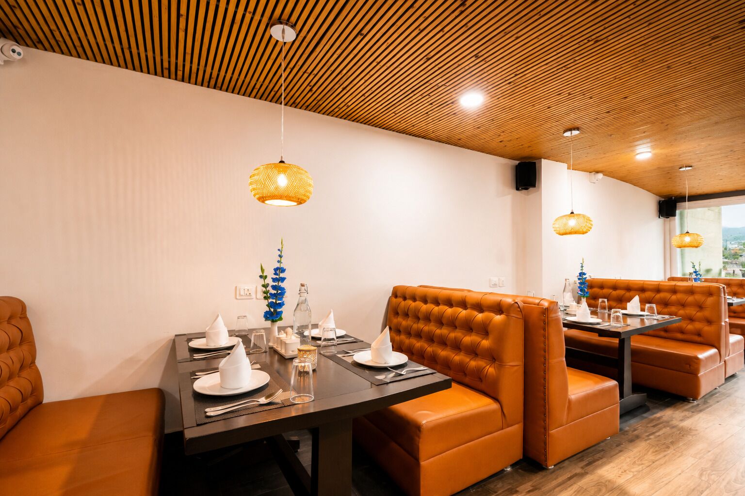 A restaurant interior with wooden ceiling, brown leather booths, and hanging wicker lamps.