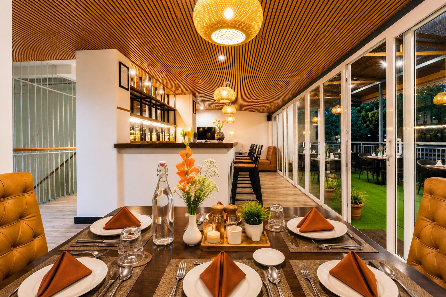 A dining area with a long table set for a meal, a bar in the background, and a view of the outdoors.