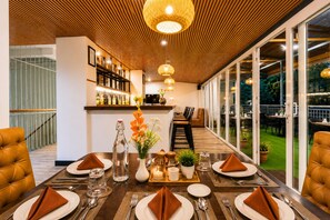 Un comedor con una mesa larga dispuesta para una comida, una barra al fondo y vistas al exterior.