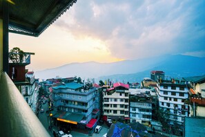 Un paisaje urbano con edificios de varios pisos, una calle con vehículos y una cadena montañosa al fondo.