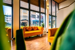 Una habitación con piso de madera, un sofá naranja brillante y amplios ventanales con vistas a edificios.