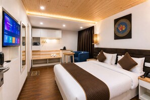 Habitación de hotel con cama, mesita de noche, un escritorio con silla, televisor y una obra de arte en la pared.