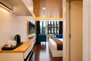 Ein Hotelzimmer mit Holzboden, einem Wandfernseher, einem Bett, einer Sitzecke mit Tisch und einem Vorhangfenster.