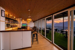 Zona de bar con techo de madera, un televisor y vistas a montañas a través de grandes puertas de cristal.