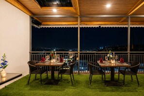A restaurant with two tables set for dining, overlooking a cityscape at night. - Sparrow Elements Boutique Near MG Marg  (Gangtok)
