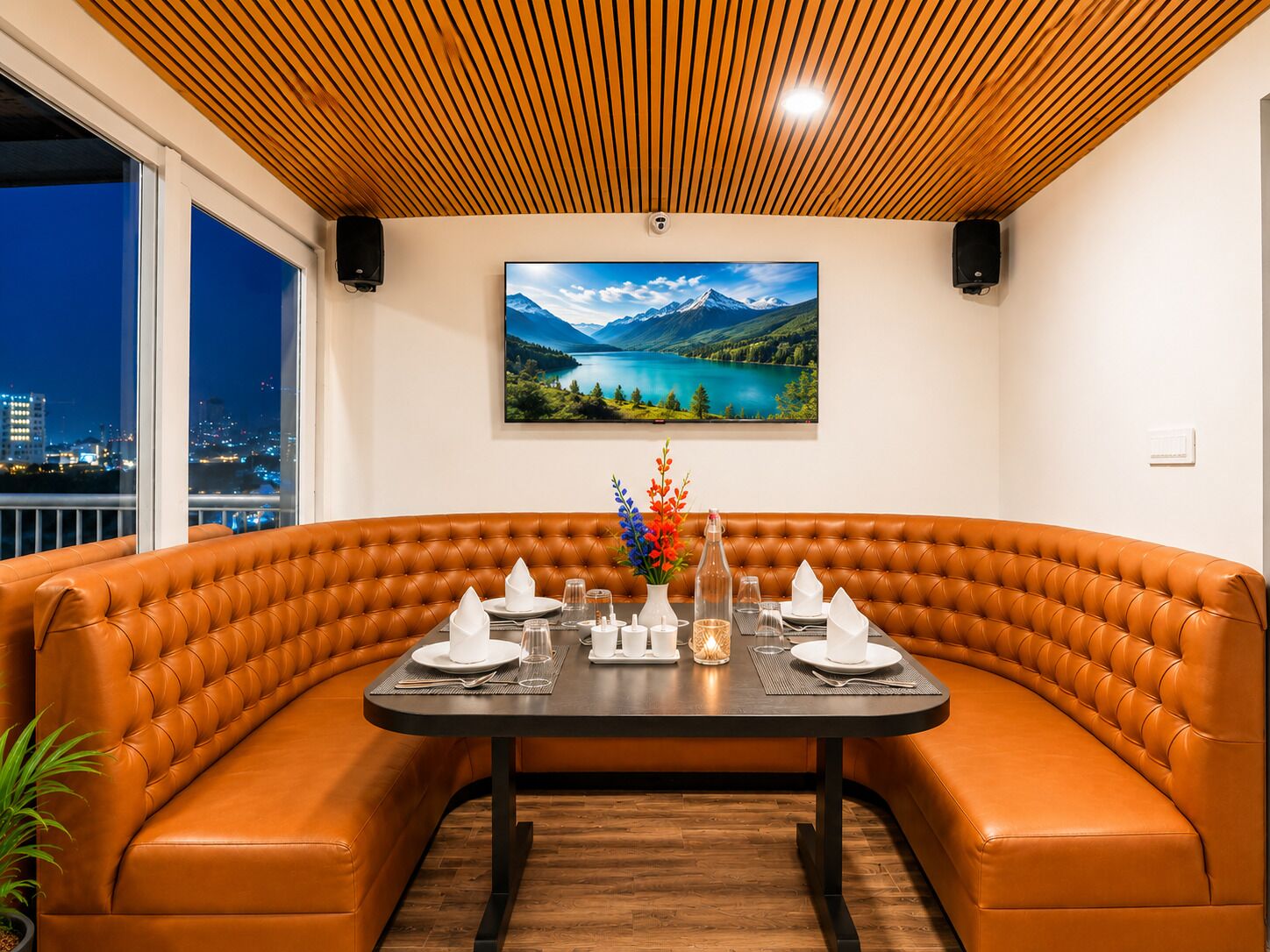A dining area with a brown leather booth, a black table set for four, and a scenic mountain lake view.
