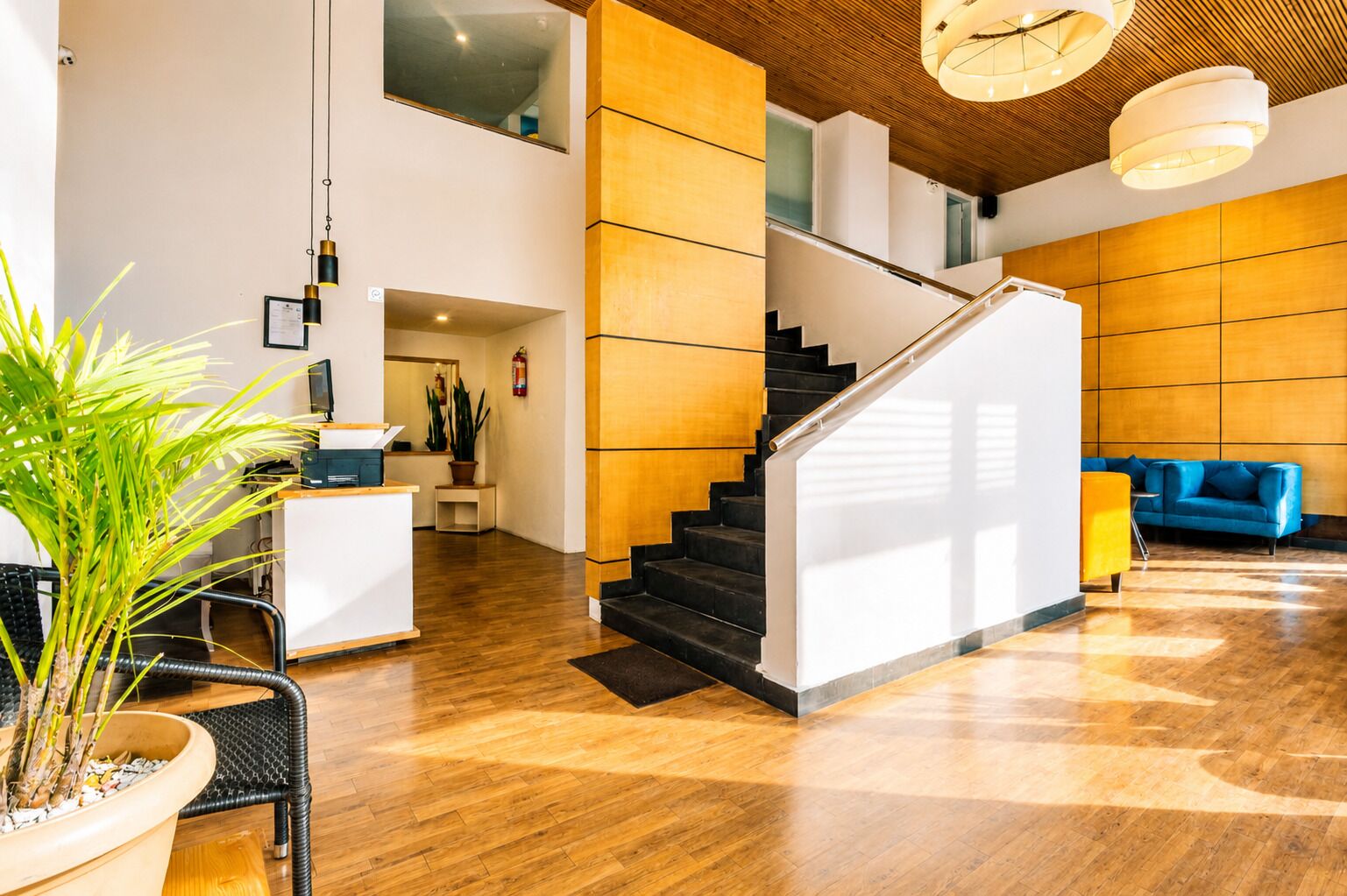 A modern hotel lobby with a wooden staircase, a reception desk, and a blue sofa.