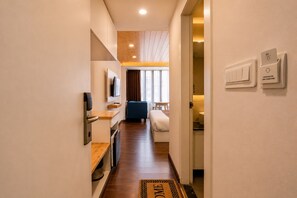 Pasillo de hotel con una cama, televisor y escritorio.