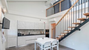 Una cocina moderna con armarios blancos, una mesa de comedor con sillas y una escalera con escalones de madera.