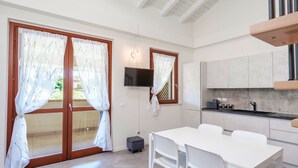 Una cocina moderna con horno empotrado, un comedor con mesa y sillas blancas, y una puerta corrediza de vidrio con cortinas.