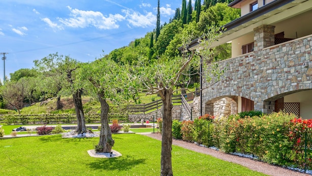Un jardín bien cuidado con un edificio de piedra, cielo despejado y un paisaje montañoso al fondo.