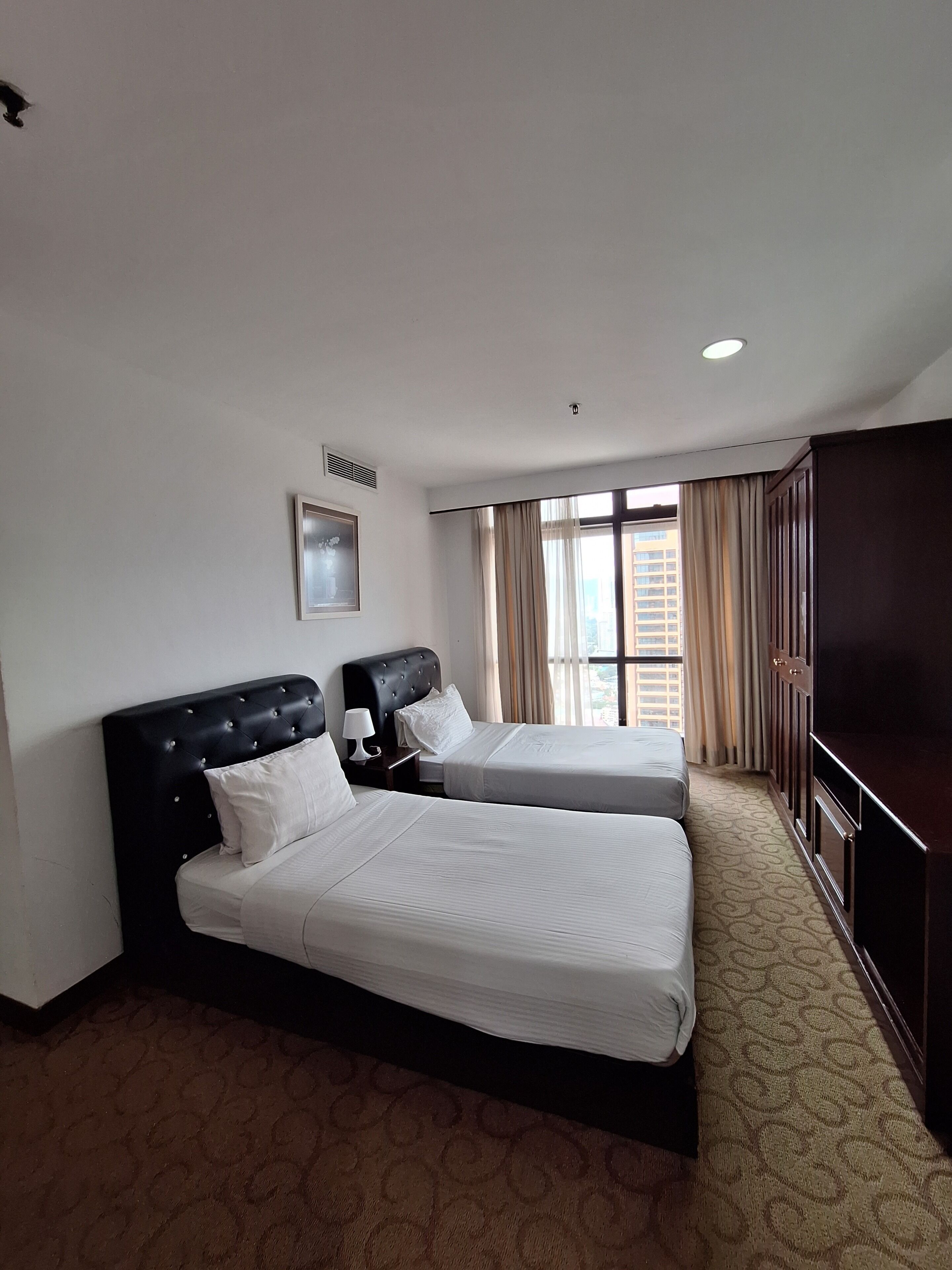 A hotel room with two beds, a television, a window with curtains, and a carpeted floor.