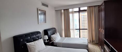 A hotel room with two beds, a television, a window with curtains, and a carpeted floor.