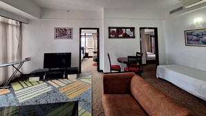 Ein Hotelzimmer mit einer Couch, einem Fernseher, einem Esstisch mit Stühlen und einem gemusterten Teppich.