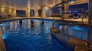 Una piscina interior con agua cristalina, suelo de baldosas y vistas a la ciudad iluminada de noche.