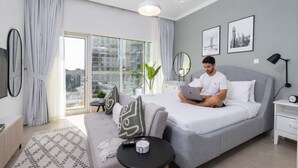 Ett modernt hotellrum med en stor säng, en soffa, ett litet bord, ett skrivbord och utsikt över staden genom stora fönster.
