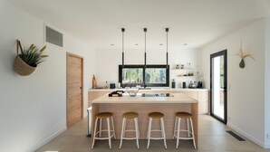 A modern kitchen with a central island, bar stools, pendant lighting, and a view through the window. - VILLA JUCA - SAINT CYPRIEN SOUTH CORSICA- 10 PERS- 5 MIN FROM THE BEACH (Zonza)