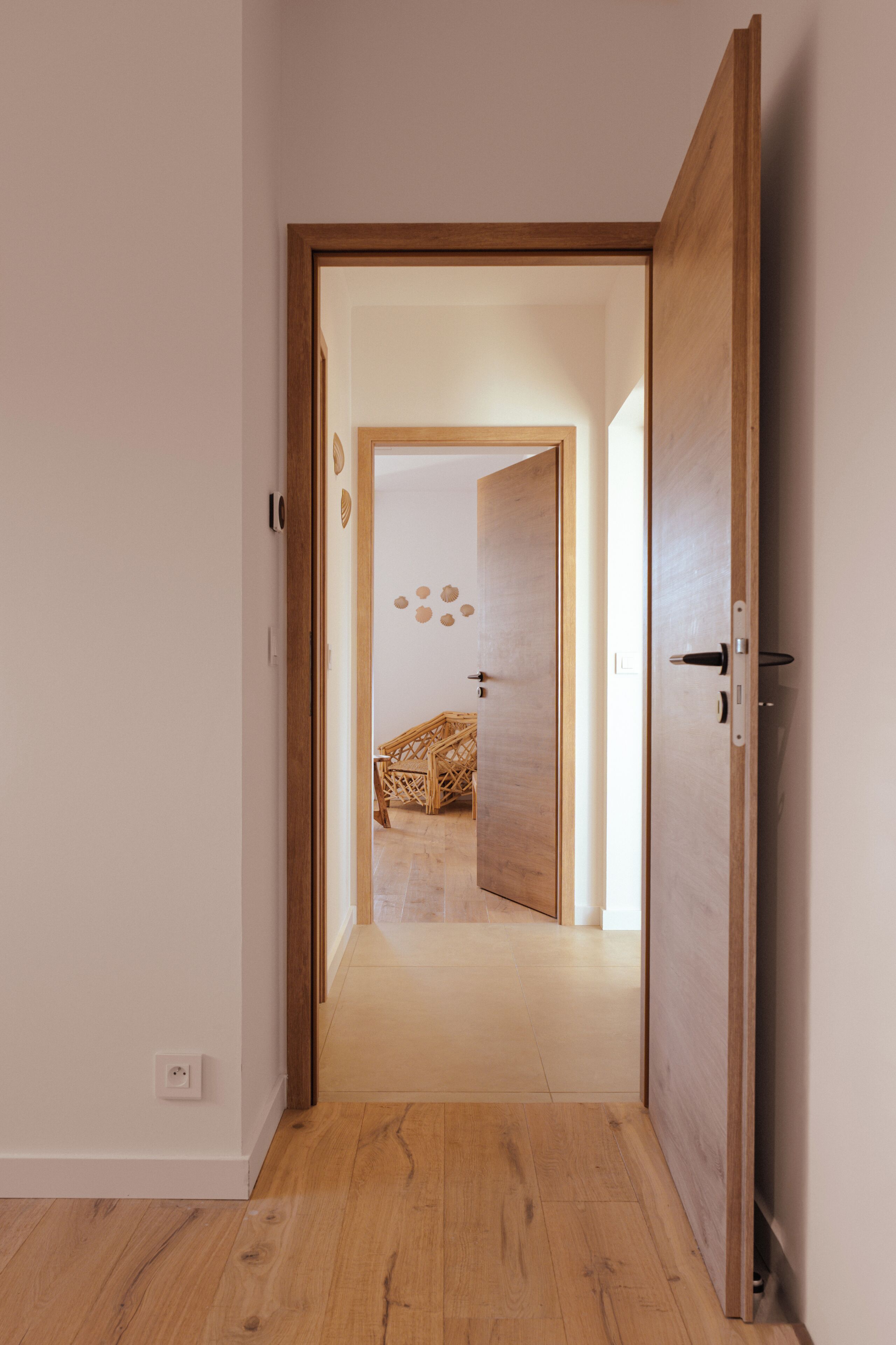 Ein Flur mit Holzboden und einer Holztür, die zu einem Raum mit einem Bett und einer Wandleuchte führt.