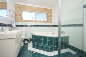 A modern bathroom with a bathtub, a glass shower enclosure, and a window above the sink. - Family Coastal Retreat With Pool and Balcony Views (Coffs Harbour)