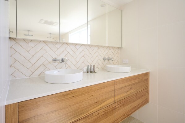 Un baño moderno con dos lavamanos, muebles de madera y salpicadero de baldosas en patrón de espiga.