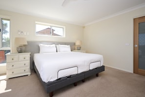 A bedroom with a bed, two bedside tables, a window, and a door. - Family Coastal Retreat With Pool and Balcony Views (Coffs Harbour)