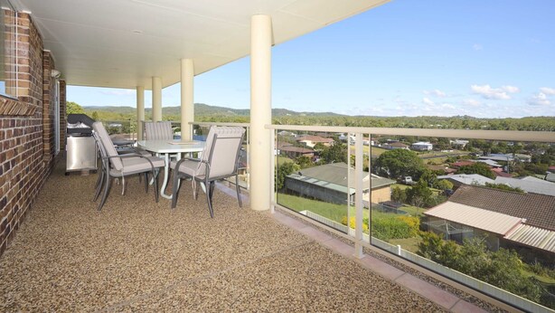 Ein überdachter Balkon mit Tisch, Stühlen, einem Grill und Blick auf ein Wohngebiet.
