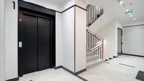 Interior moderno com elevador preto, escada com corrimãos de madeira e piso revestido de azulejos.