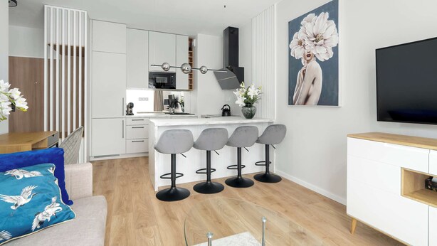 Cozinha moderna com armários brancos, ilha central com banquetas, televisão de tela plana e um grande quadro floral na parede.