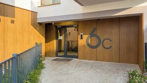 Entrada de um edifício moderno com fachada de madeira, porta de vidro e uma placa com o número '6c'.