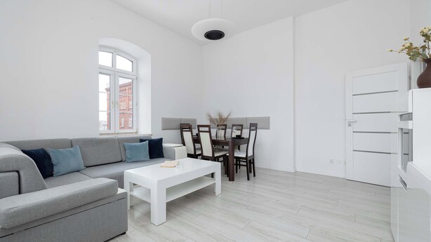 Ett modernt vardagsrum med en grå soffa, ett vitt soffbord och en matplats med ett bord och stolar.