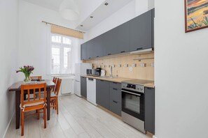 A modern kitchen with grey cabinets, a wooden countertop, and a dining area with a table and chairs. - Family Suite | 3 Bedrooms, Workspace (Kołobrzeg)