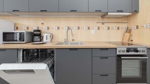 Ett modernt kök med gråa skåp, en mikrovågsugn, en kaffebryggare, en diskho och en ugn.