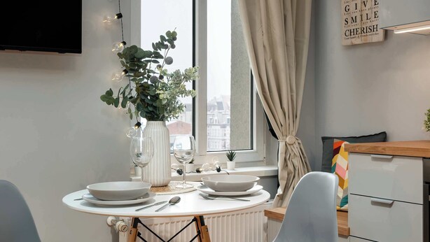 A dining area with a round table set for two, a vase with flowers, and a window with curtains. - Climatic Studio in the Center | Close to Public Transport (Bydgoszcz)