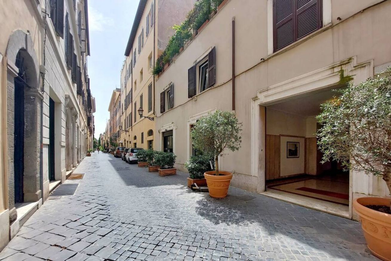 Une ruelle étroite pavée, bordée de bâtiments historiques, de plantes en pot et sous un ciel dégagé.
