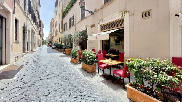 A narrow cobblestone street lined with buildings, outdoor seating with red chairs and tables, and potted plants. - MARGUTTA LOFT FOR SMART WORKER (Roma)