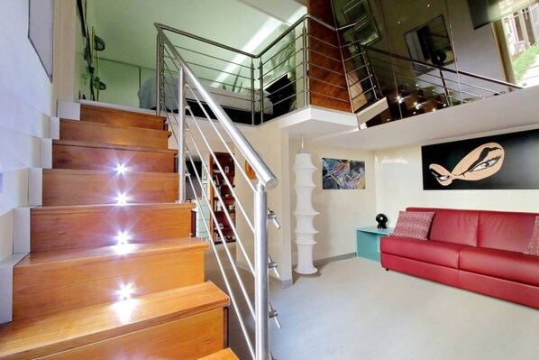 A modern interior with a wooden staircase, a red sofa, and a painting of an eye on the wall. - MARGUTTA LOFT FOR SMART WORKER (Roma)