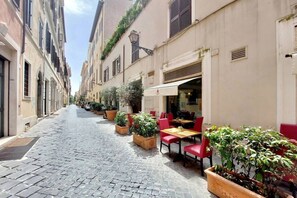 A narrow cobblestone street lined with buildings, outdoor seating with red chairs and tables, and potted plants. - MARGUTTA LOFT FOR SMART WORKER (Roma)