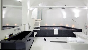 A modern bathroom with a large mirror, a black bathtub, a white sink, and a shower area. - Cloud 9 (Santorini)