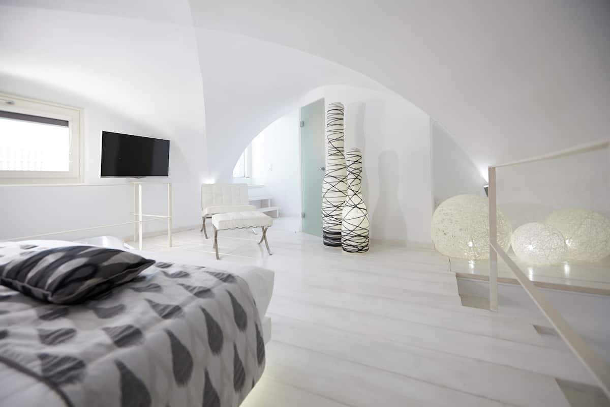 A modern bedroom with a bed, a TV, a chair, and decorative vases.