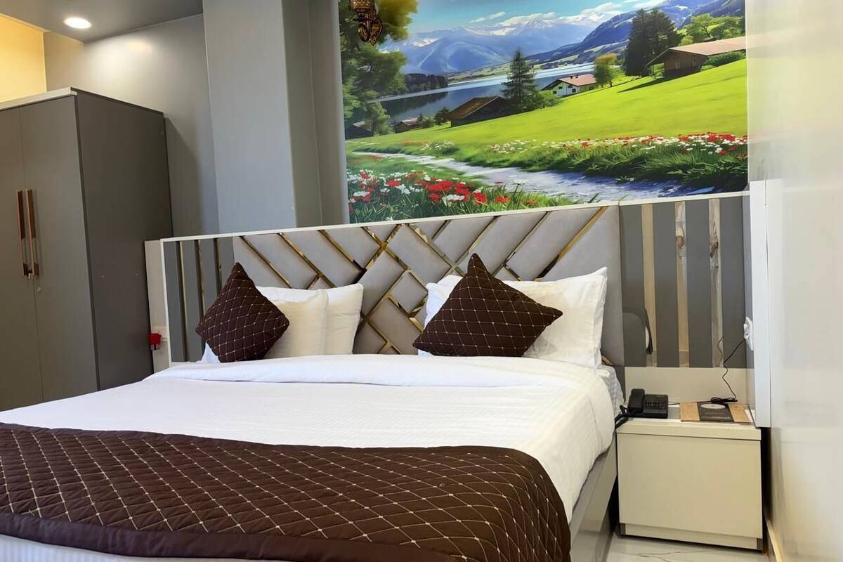 Una habitación de hotel con una cama grande, una mesita de noche con un teléfono y un libro, y un mural de un paisaje en la pared.