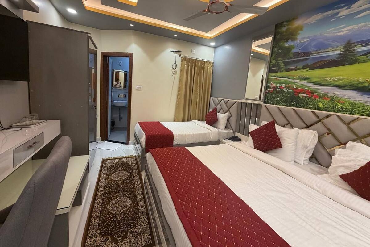 Habitación de hotel con dos camas, un escritorio, una silla, un ventilador de techo y un cuadro en la pared.