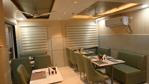 A restaurant with booths and tables, ceiling fans, and a modern design. - Hotel Aveda Paradise (Varanasi)