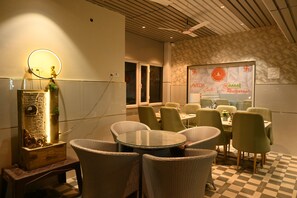 Ein Restaurantinnenraum mit runden Tischen, grünen Stühlen, einem Schachbrettmuster-Boden und einer an der Wand befestigten Speisekarte.