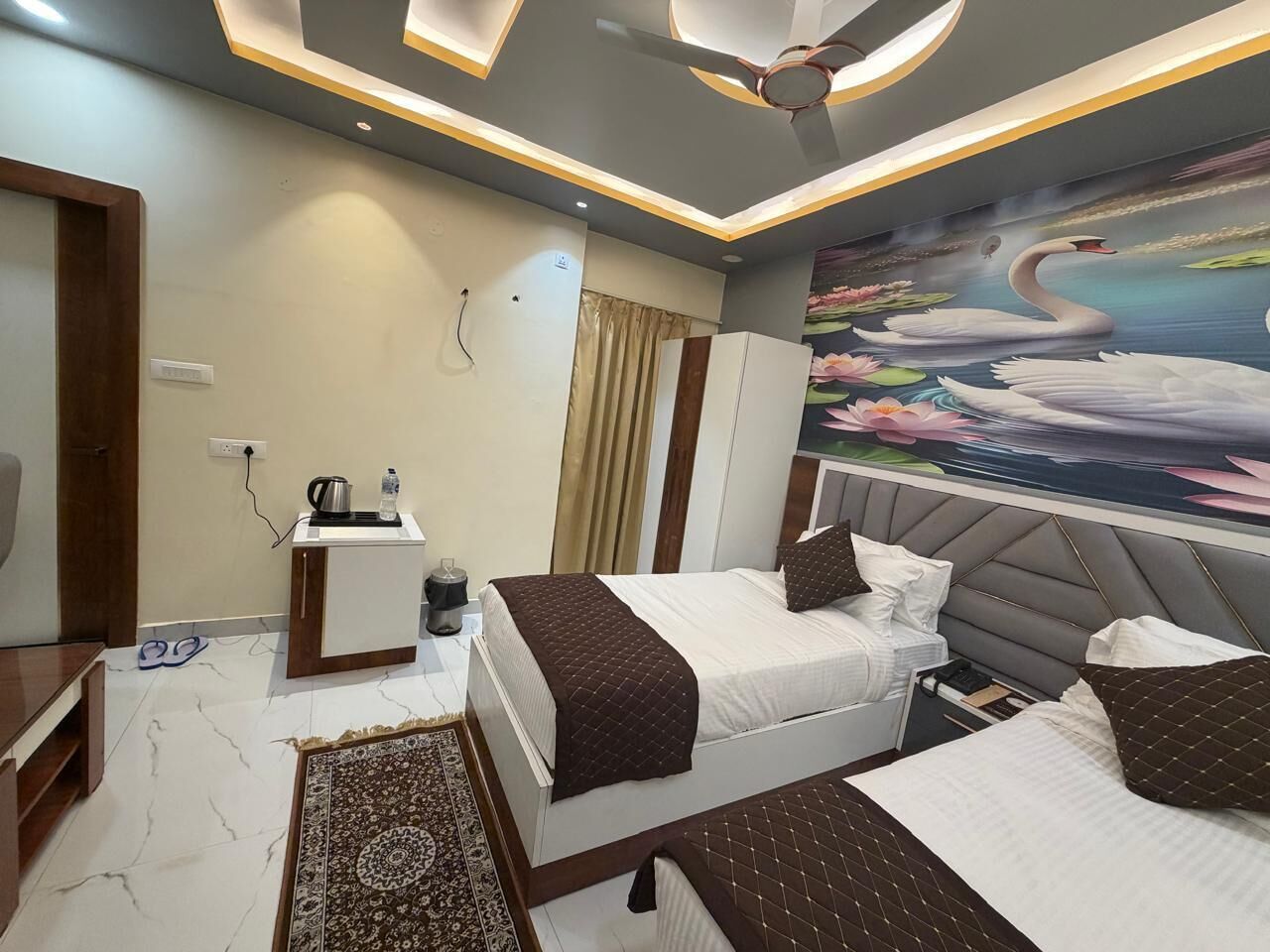 Ein modernes Hotelzimmer mit zwei Betten, einem Schreibtisch, einem Deckenventilator und einem Wandgemälde mit Schwänen.