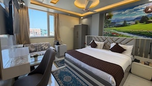 A modern hotel room with a large bed, a desk with a chair, a wardrobe, and a view of a green landscape through the window. - Hotel Aveda Paradise (Varanasi)